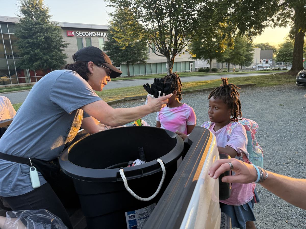 A volunteer leaning over a supply bin to hand something to two young girls at a distribution
