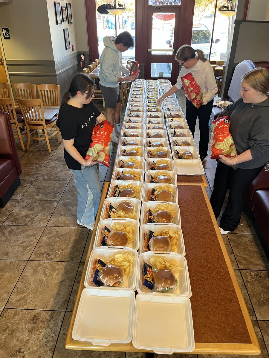 Rows of prepared meal trays laid out down the length of a restaurant dining room